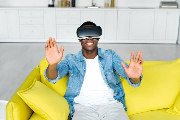 Vista de ángulo alto del hombre afroamericano feliz en auriculares vr sentado en el sofá - foto de stock