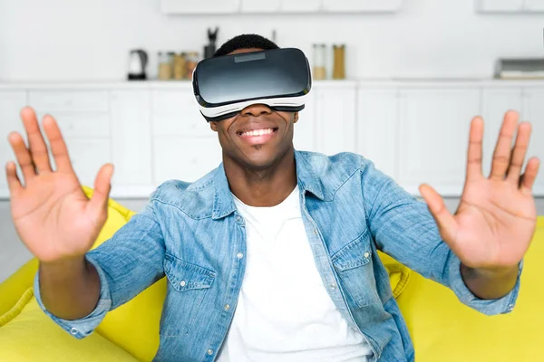 Hombre afroamericano feliz en auriculares vr sentado en el sofá - foto de stock