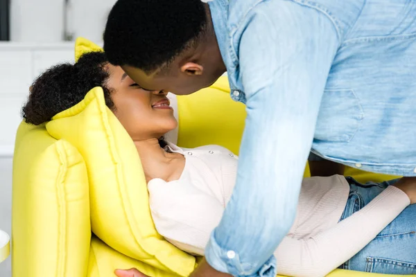 African american man kissing girlfriend on couch — Stock Photo