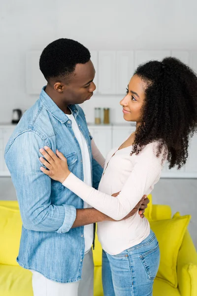 Vista lateral de la pareja afroamericana mirándose, de pie en habitación luminosa - foto de stock