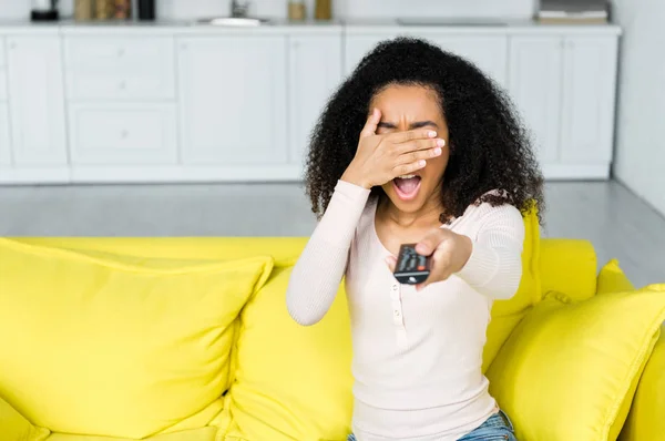 Donna afroamericana con telecomando in mano che copre il viso — Foto stock