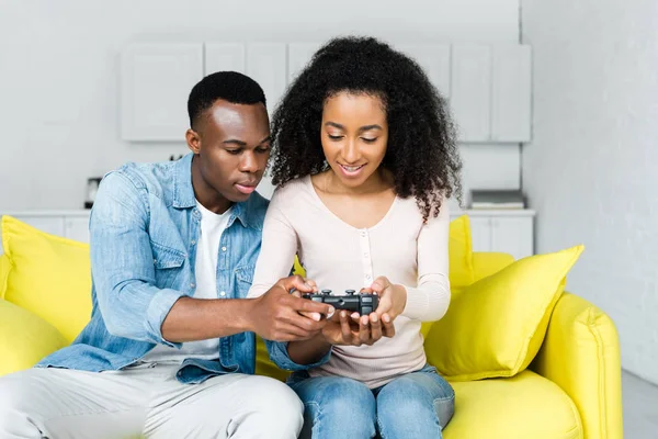 KYIV, UCRAINA - 13 MAGGIO 2019: coppia afroamericana che tiene in mano il gamepad, seduta sul divano — Foto stock
