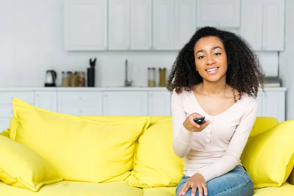 Cheerful african american woman holding remote controller in hand and looking at camera — Stock Photo