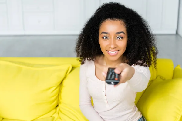 Vue grand angle de femme afro-américaine heureuse tenant la télécommande à la main — Photo de stock