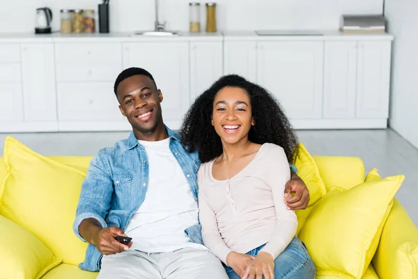 Alegre pareja afroamericana pasar tiempo juntos en casa con mando a distancia en la mano - foto de stock