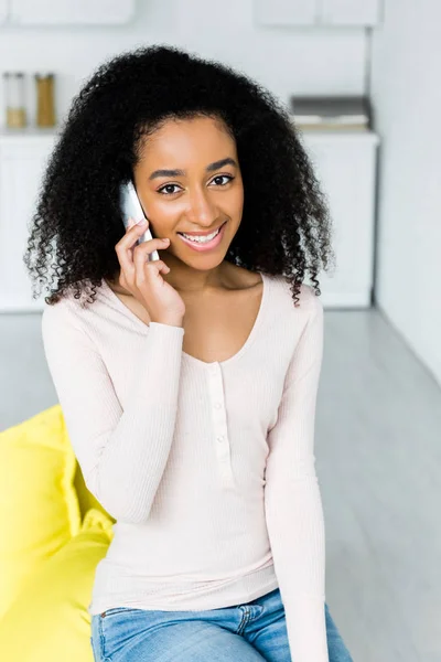 Mujer afroamericana feliz hablando en el teléfono inteligente, y mirando la cámara - foto de stock