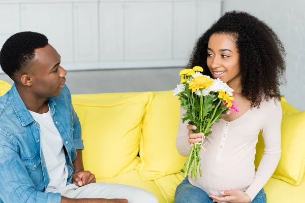 Enceinte afro-américaine tenant des fleurs dans la main, et en regardant petit ami — Photo de stock