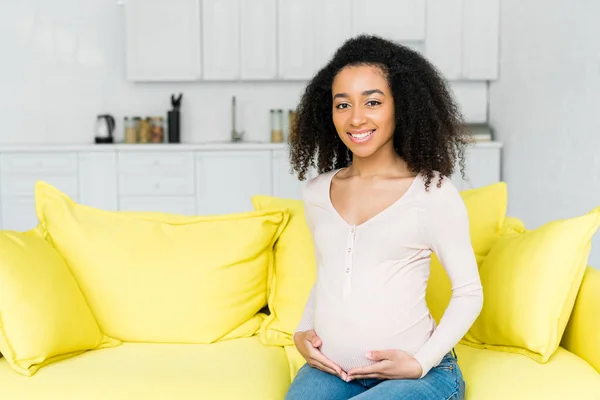 Pregnant african american woman sitting on couch at home — Stock Photo