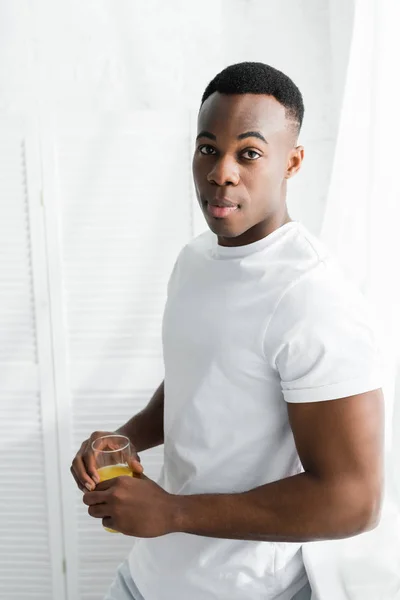 Hombre afroamericano sosteniendo vaso con jugo de naranja en las manos - foto de stock