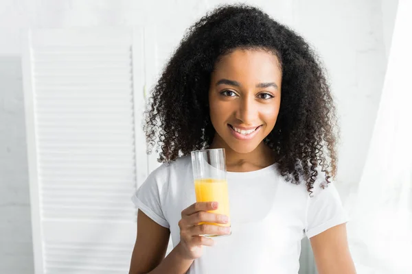 Happy african american woman with glass of juice looking at camera — Stock Photo