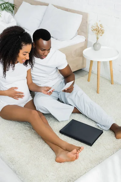 Alto ángulo vista de embarazada africana americana mujer mirando foto con novio - foto de stock
