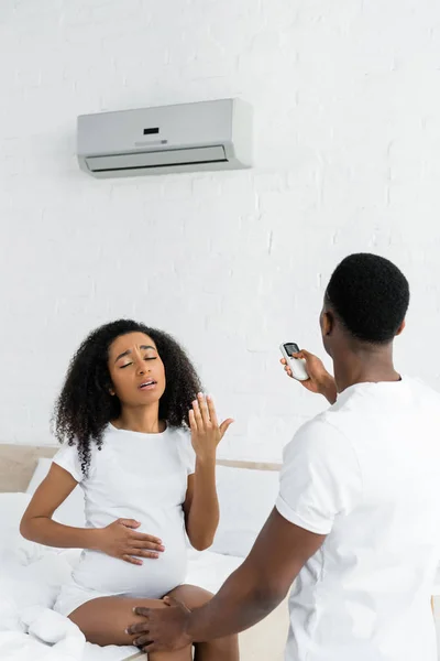 Hombre afroamericano encendiendo el aire acondicionado para la esposa embarazada - foto de stock