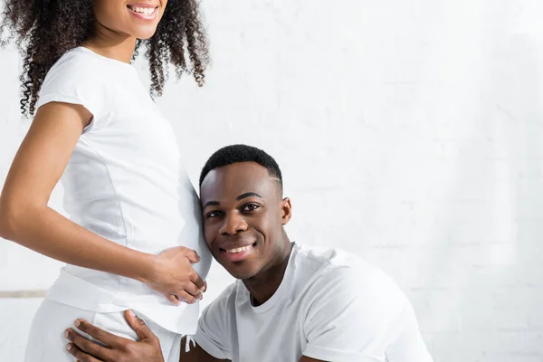 Vista cortada do homem afro-americano ouvindo barriga grávida esposa — Fotografia de Stock