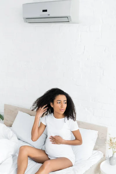 Pregnant african american woman sitting under air conditioner and looking away — Stock Photo