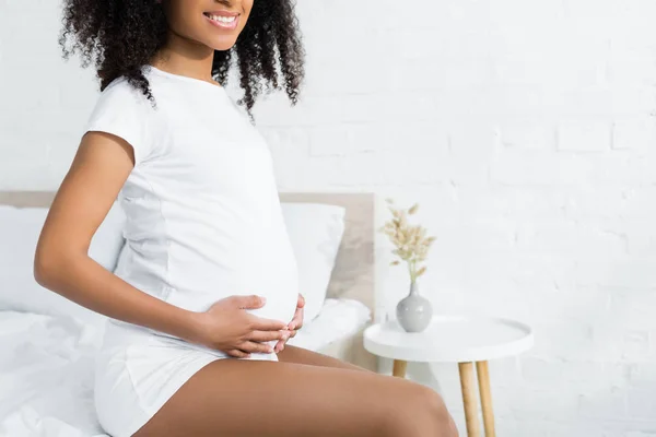 Vista recortada de la mujer afroamericana feliz y embarazada en la habitación - foto de stock