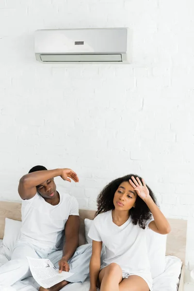 Vista de ángulo alto de la pareja afroamericana sentada en la cama en la habitación con aire acondicionado - foto de stock