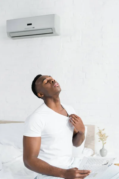 Hombre afroamericano agotado en la habitación con temperatura de calor y aire acondicionado - foto de stock