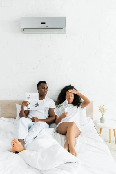 Африканская американская пара, сидящая на кровати в комнате с температурой тепла, и кондиционер — стоковое фото