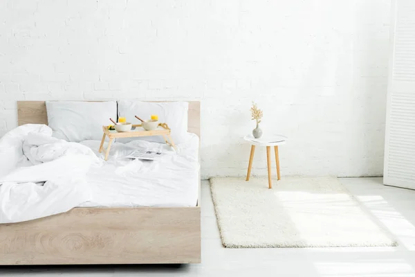 Plateau de table avec petit déjeuner au lit dans une chambre blanche et lumineuse — Photo de stock