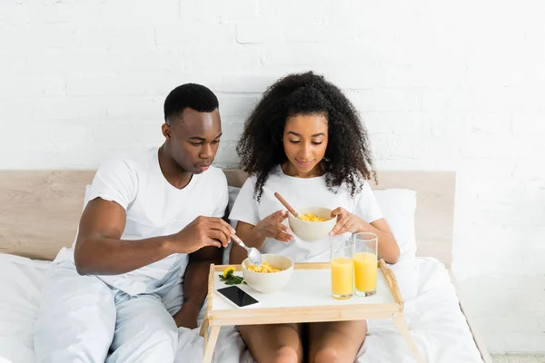 Heureux et calme couple afro-américain manger le petit déjeuner au lit — Photo de stock