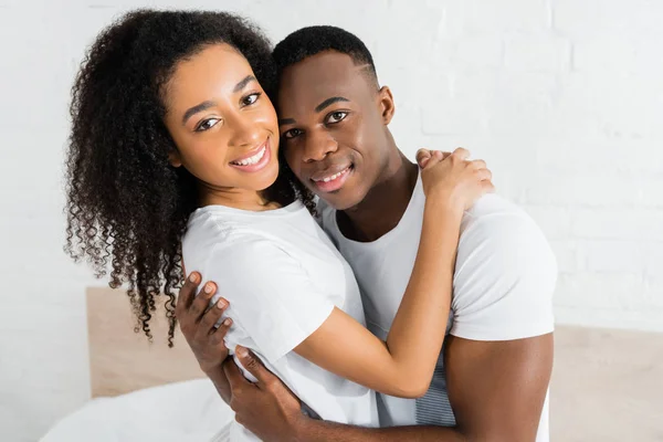 Africano americano pareja abrazándose unos a otros y mirando la cámara - foto de stock