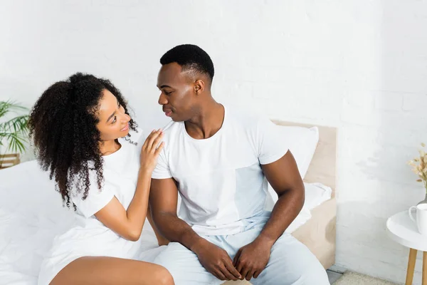 Vista de ángulo alto de la pareja afroamericana sentada en la cama y mirándose - foto de stock