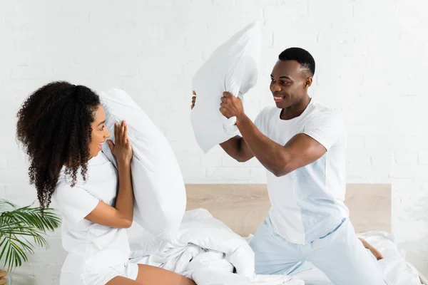 Afrikanisch-amerikanisches Paar kämpft auf dem Bett mit Kissen in den Händen — Stockfoto