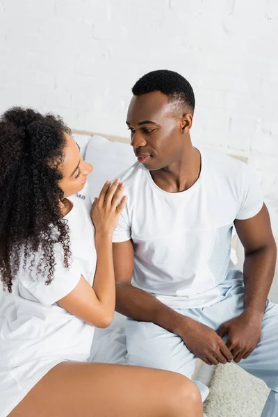 Vista de ángulo alto de la pareja afroamericana mirándose, sentados en la cama - foto de stock