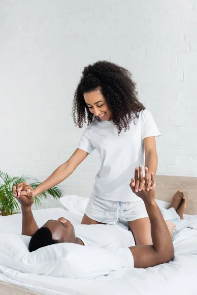 African american man lying on bed, holding hands with girlfriend — Stock Photo