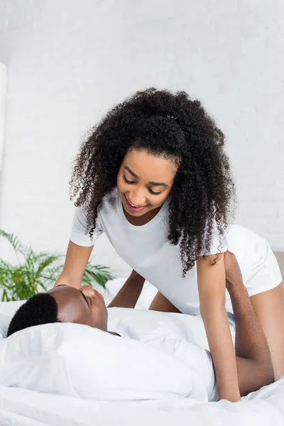 Atractiva mujer afroamericana mirando novio, pasando la mañana en la cama - foto de stock