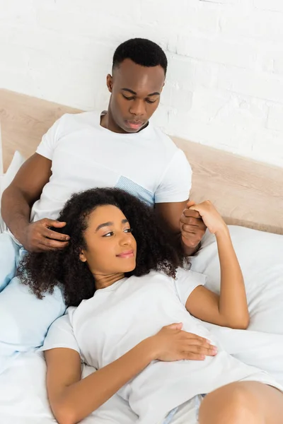 High angle view of african american man holding hands with beautiful girlfriend, lying on bed — Stock Photo