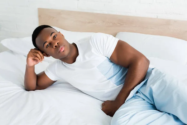 High angle view of african american man lying on bed, looking at camera — Stock Photo