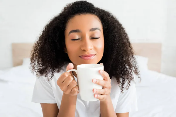 Portrait d'une femme afro-américaine fermant les yeux, tenant une tasse avec une boisson dans les mains — Photo de stock