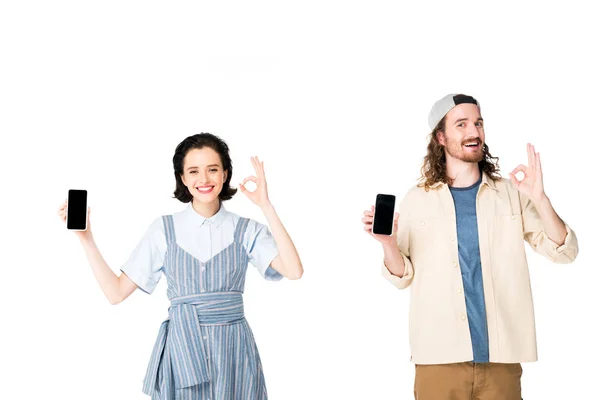 Молодая пара держит в руках смартфоны и показывает ОК знаки изолированы на белом — стоковое фото