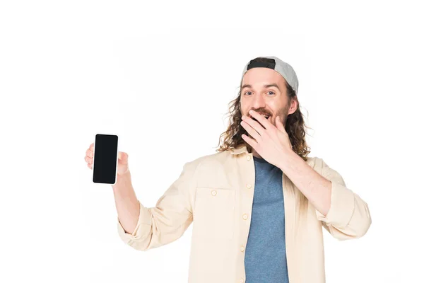 Excité jeune homme tenant smartphone et fermeture de la bouche avec la main isolée sur blanc — Photo de stock