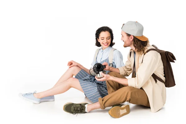 Young couple of tourists sitting and man pouring cup from thermos isolated on white — Stock Photo