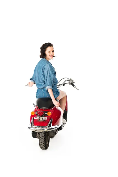 Ganzkörperansicht des Mädchens, das in die Kamera schaut und lächelt, während es auf einem roten Motorroller sitzt, isoliert auf weißem Grund — Stockfoto