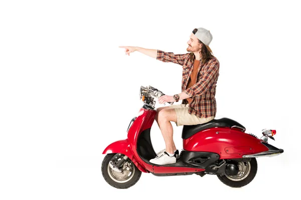 Vista laterale del giovane seduto su scooter rosso e puntando con il dito isolato su bianco — Foto stock