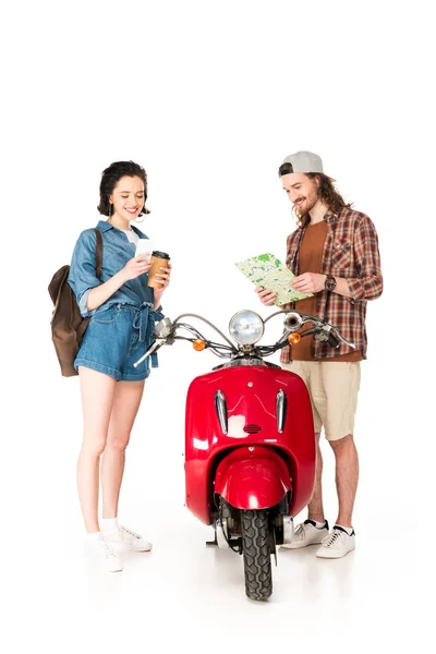 Девушка в полный рост смотрит на самокат и держит в руках бумажную чашку кофе, а молодой человек смотрит на карту, стоя возле красного скутера на белом — стоковое фото