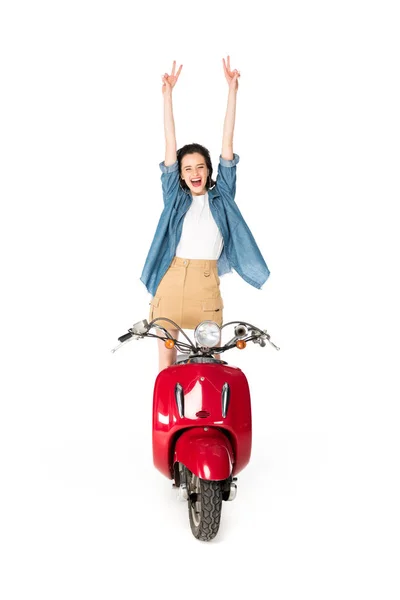 Повний вигляд дівчини, що стоїть на червоному скутері і показує знак миру ізольований на білому — стокове фото