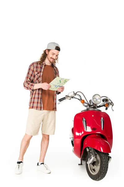 Vista completa del joven sosteniendo el mapa, de pie cerca de scooter rojo aislado en blanco — Stock Photo