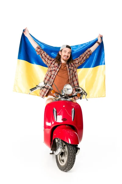 Visão comprimento total do jovem sentado em scooter vermelho, segurando bandeira ucraniana no ar isolado no branco — Fotografia de Stock