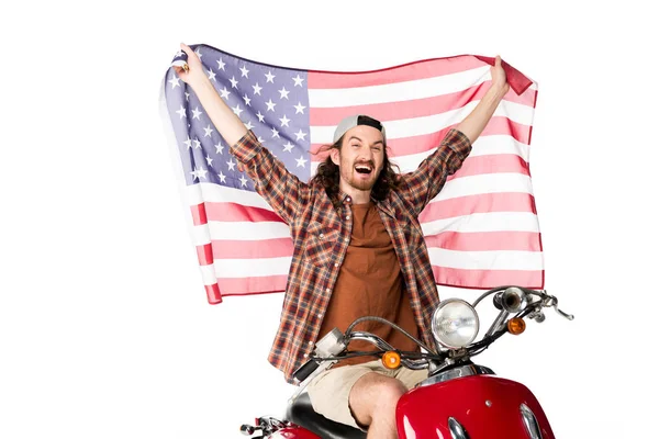 Animado jovem sentado em scooter vermelho e segurando bandeira americana no ar isolado no branco — Fotografia de Stock