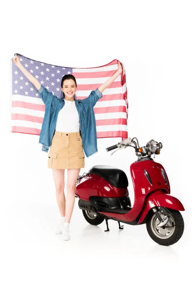 Visão comprimento total da menina bonita de pé perto de scooter vermelho e segurando bandeira americana isolada no branco — Fotografia de Stock