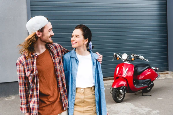 Jeune homme et fille debout près de scooter rouge et câlin — Photo de stock