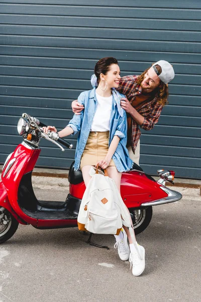 Menina bonita sentada em scooter vermelho e jovem olhando para ela — Fotografia de Stock