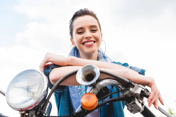 Baixo ângulo de visão da menina bonita sentado em scooter, descansando, olhando para a câmera e sorrindo no fundo do céu — Fotografia de Stock