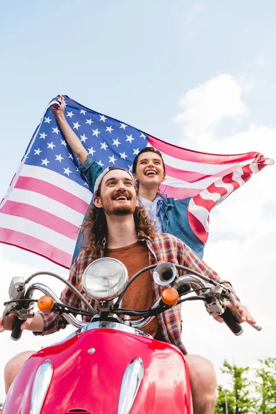 Low angle view of beautiful girl standing behind young man and holding flag on sky background — Stock Photo