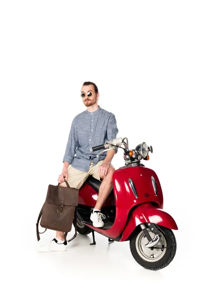 Vue pleine longueur de beau jeune homme élégant assis sur scooter rouge et tenant sac à dos isolé sur blanc — Photo de stock