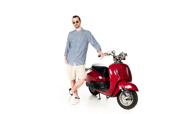 Vue pleine longueur de beau jeune homme élégant debout près de scooter rouge et regardant la caméra isolée sur blanc — Photo de stock